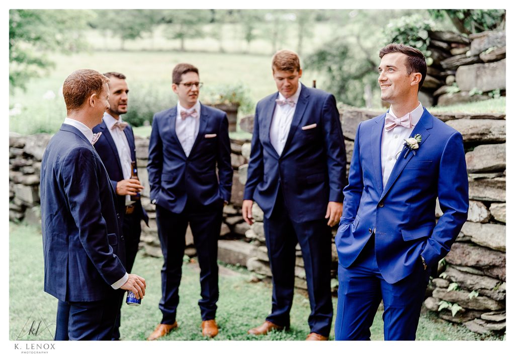 Light and Airy candid photo of a groom and his groomsmen standing next to a stone wall at the Inn at the Round Barn. 