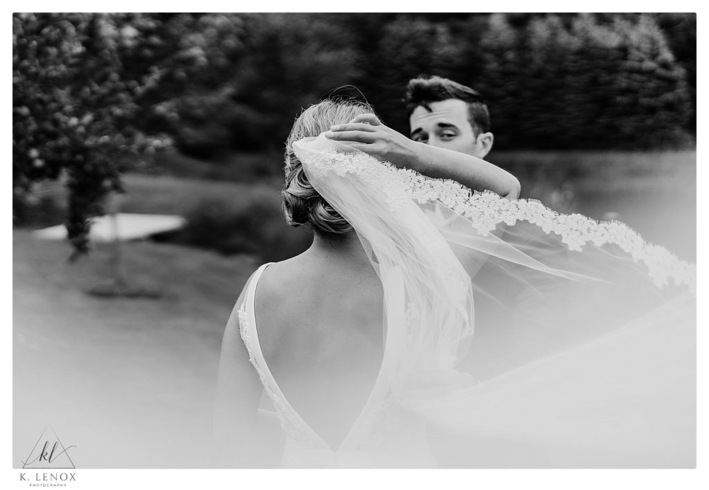 Candid and Photojournalistic black and white photo of a bride and groom laughing on their wedding day as the Bride's Veil gets blown off by the wind.