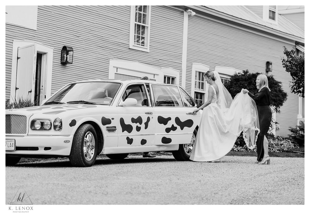 Black and White photo showing the Bride getting into a cow spotted Bentley and leaving the Inn at the Round barn for her wedding in Waterbury VT. 