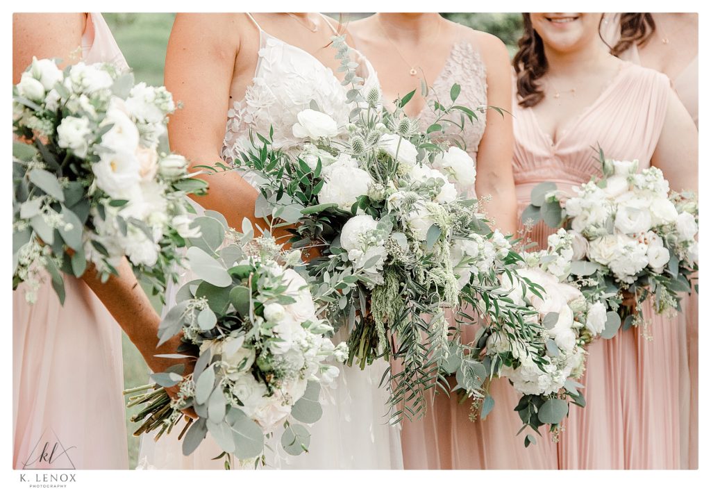 Detail photo showing bridesmaids holding their bridal bouquets with white flowers and lots of greenery. 