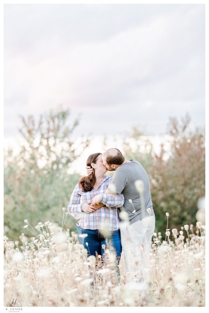 Light and Airy Engagement Session at Alyson's Orchard showing a man and woman kissing in a field of wheat like grasses. 
