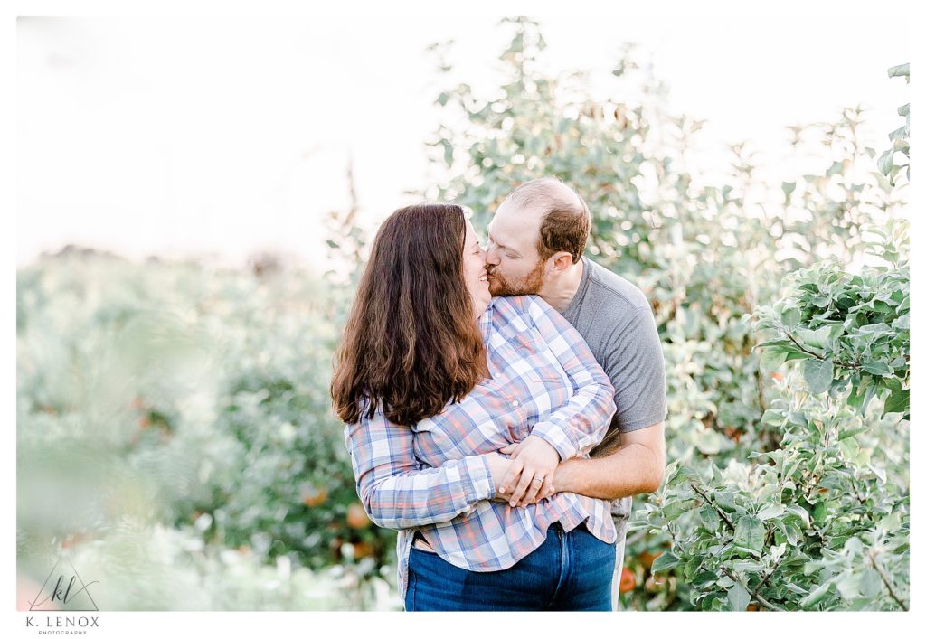 Light and Airy Engagement Session at Alyson's Orchard showing a man and woman kissing in the orchard trees. 