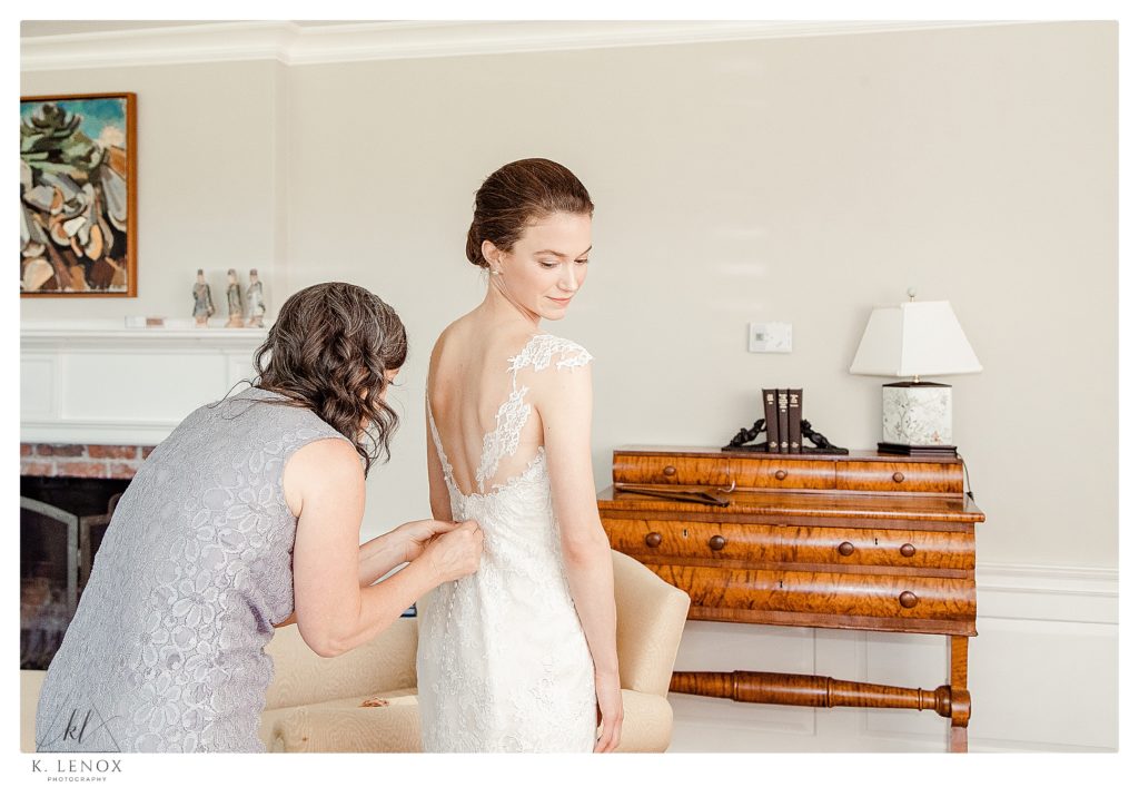 A bride gets into her wedding dress as her mom helps her button it up. 