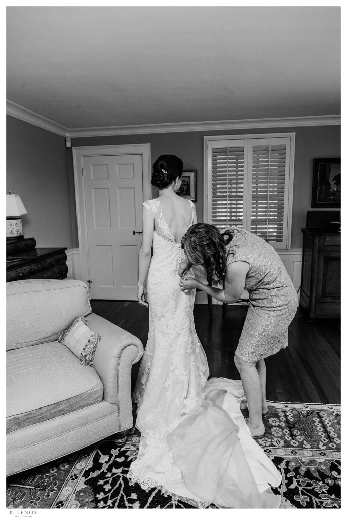 Black and white photo of a bride and her mom helping her button her wedding dress on her wedding day. 