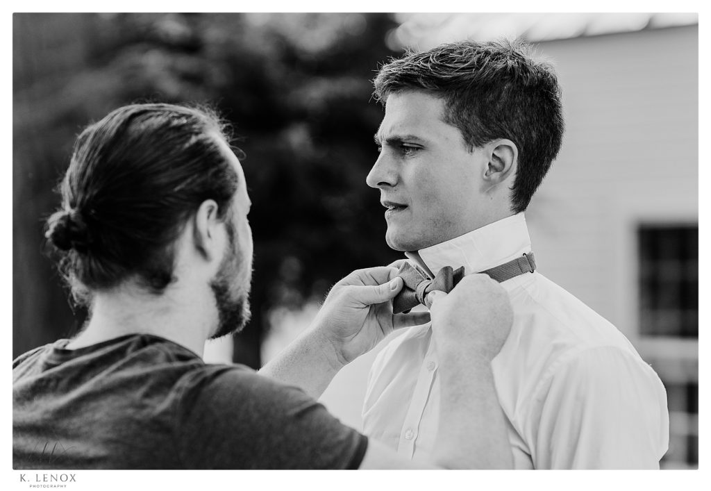 Black and White Photo of a Groom getting his bow tie tied by his friend.  Simple Tamworth NH Wedding
