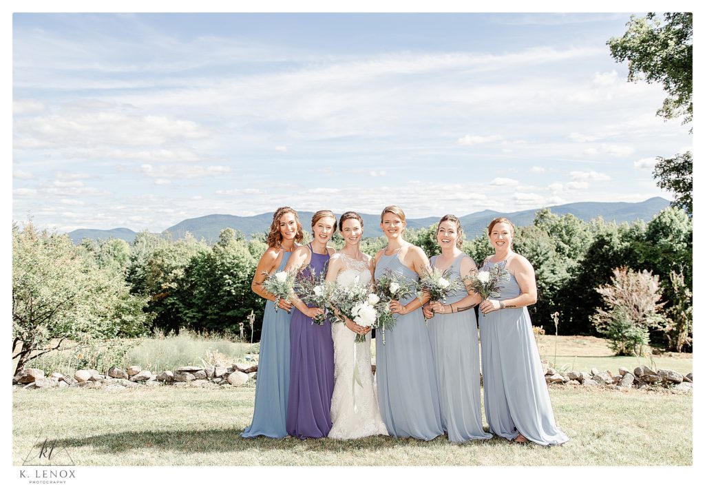 A bride and her bridesmaids wearing light blue dresses pose for a photo overlooking the Mountains of Tamworth NH.  