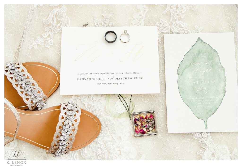 Light and Airy wedding day details showing a White invitation, wedding rings and shoes on the wedding dress. 