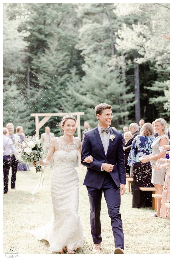 Bride and Groom walk down the aisle as their guests throw flower petals , outdoors for a simple Tamworth NH Wedding