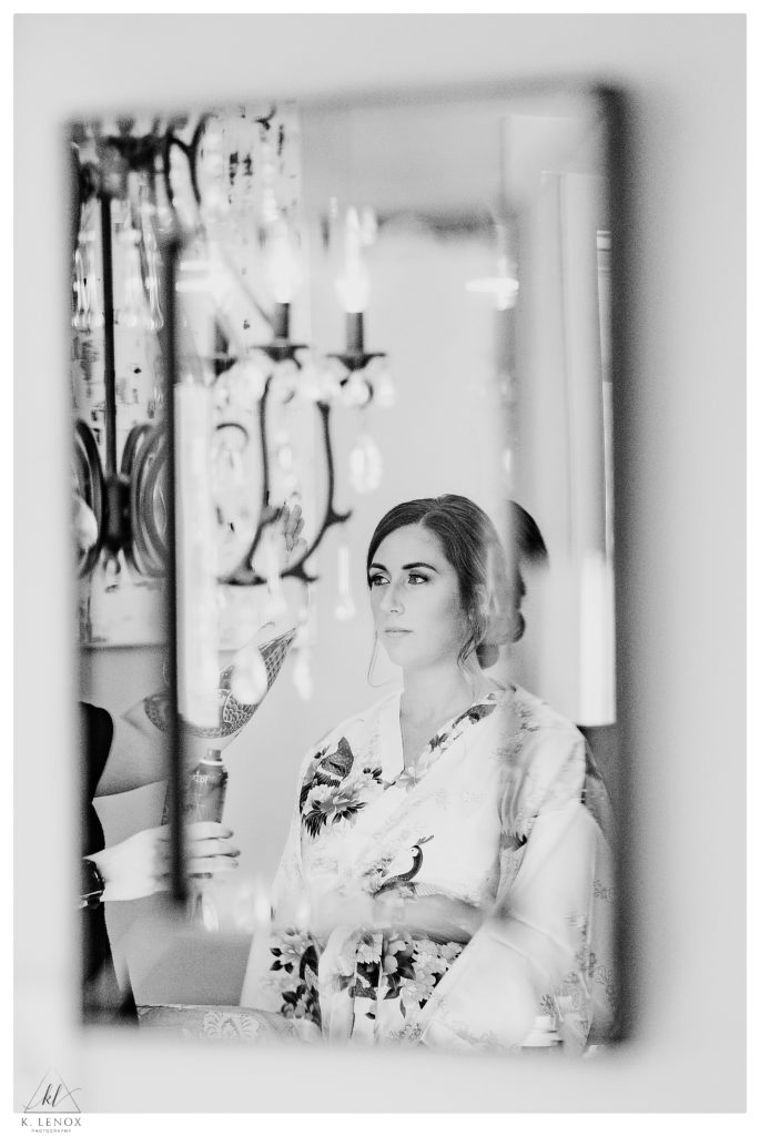 Black and White, artistic photo of a bride wearing a floral silk robe looking into a mirror on her wedding day. 