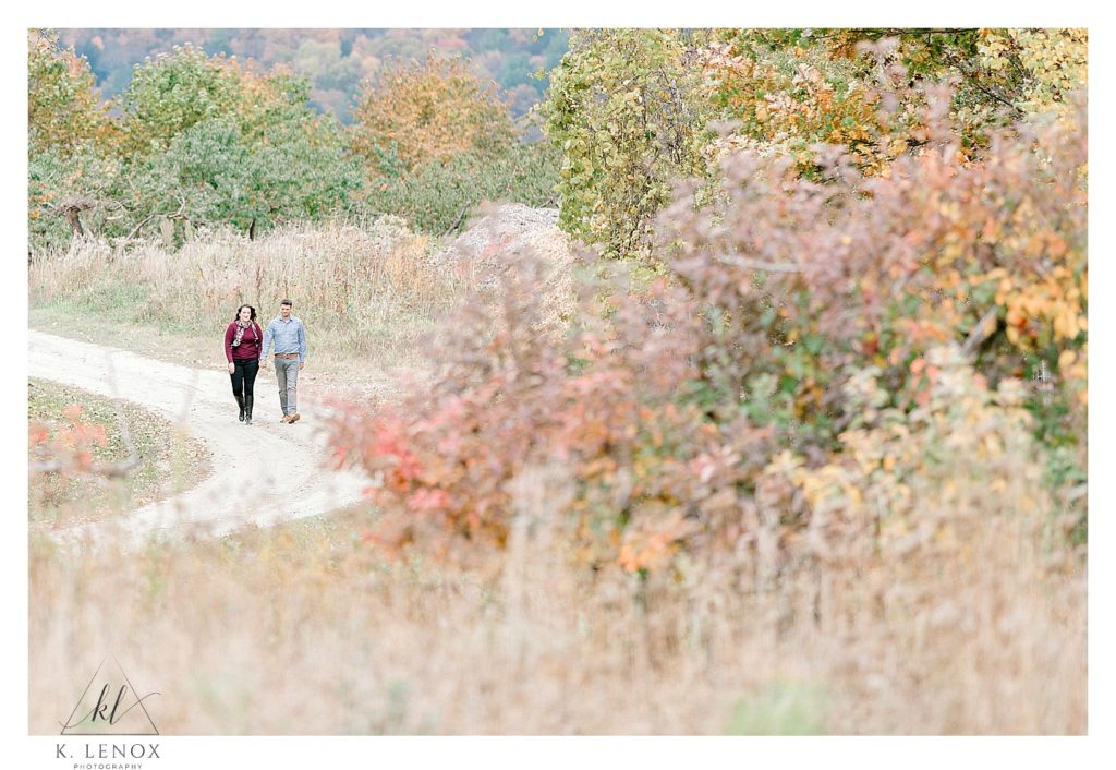 Fall Engagement Session in the Orchard- Couple walking on a dirt path in the middle of the orchard. 
