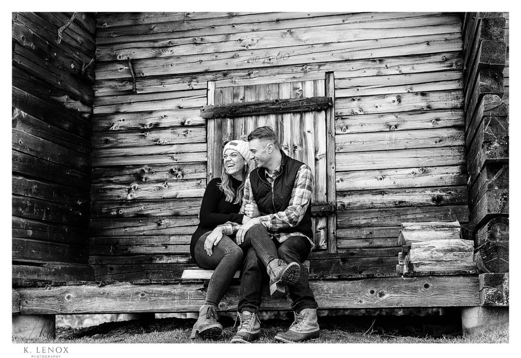 Black and white photo showing a man and woman sitting on a wooden porch at Alyson' Orchard during their engagement session! 