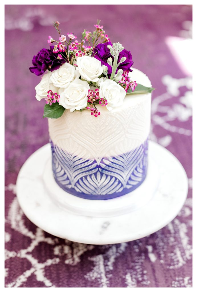 Simple One tier wedding cake for a Covid-19 Elopement.  Cake is white and purple and adorned with flowers. 