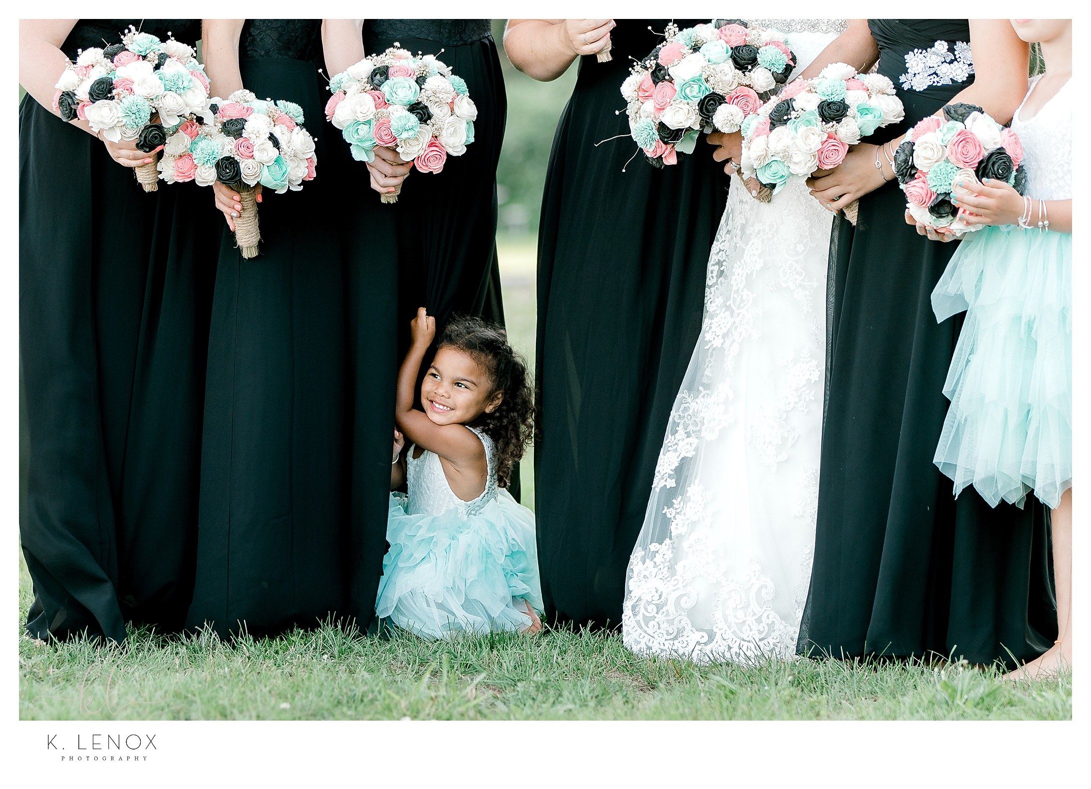 Cute little flower girl wearing a teal and white dress next to the bridesmaids wearing black. 