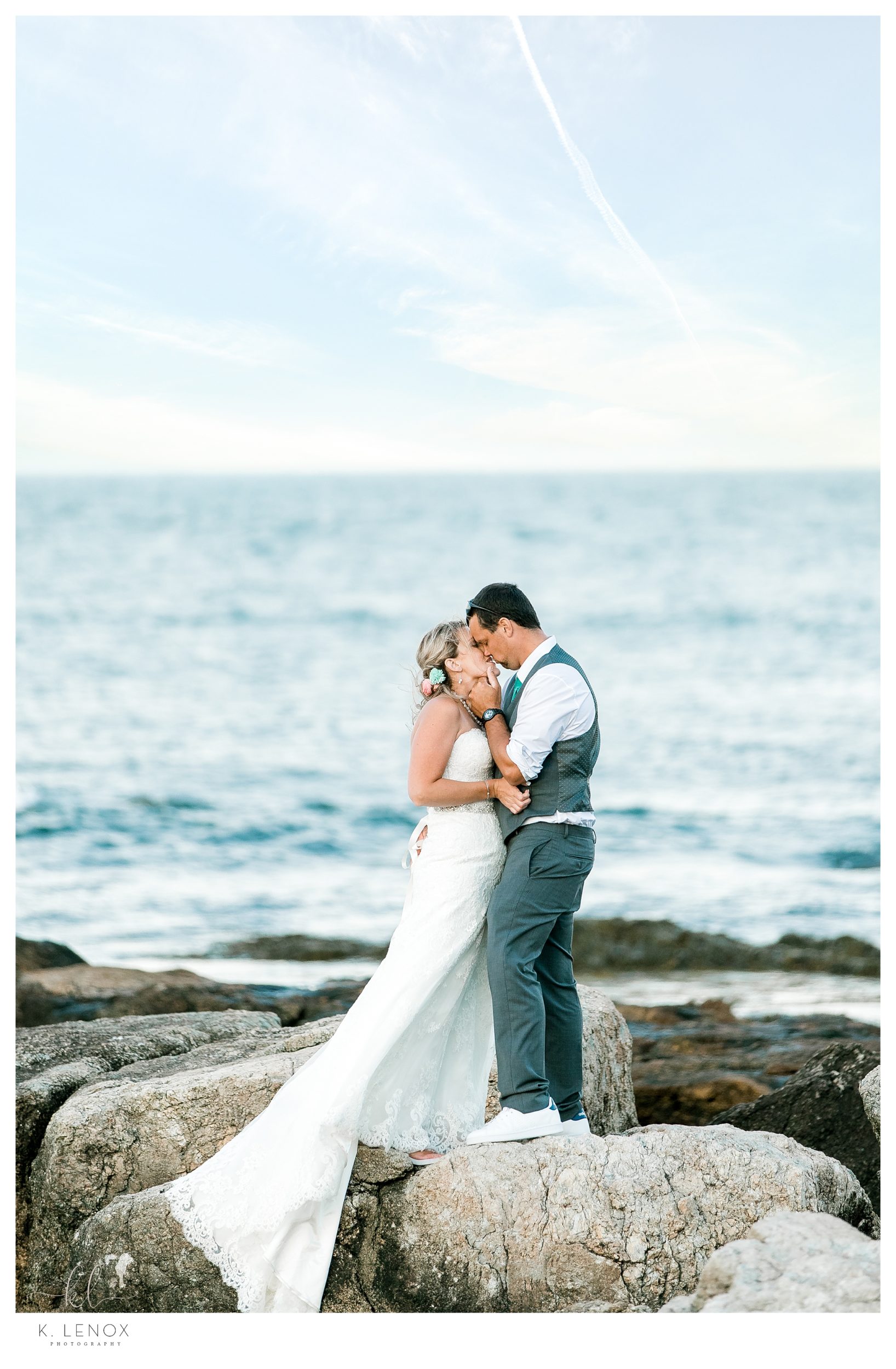 Romantic photo of a bride and groom kissing on the rocks overlooking the ocean after their seacoast wedding