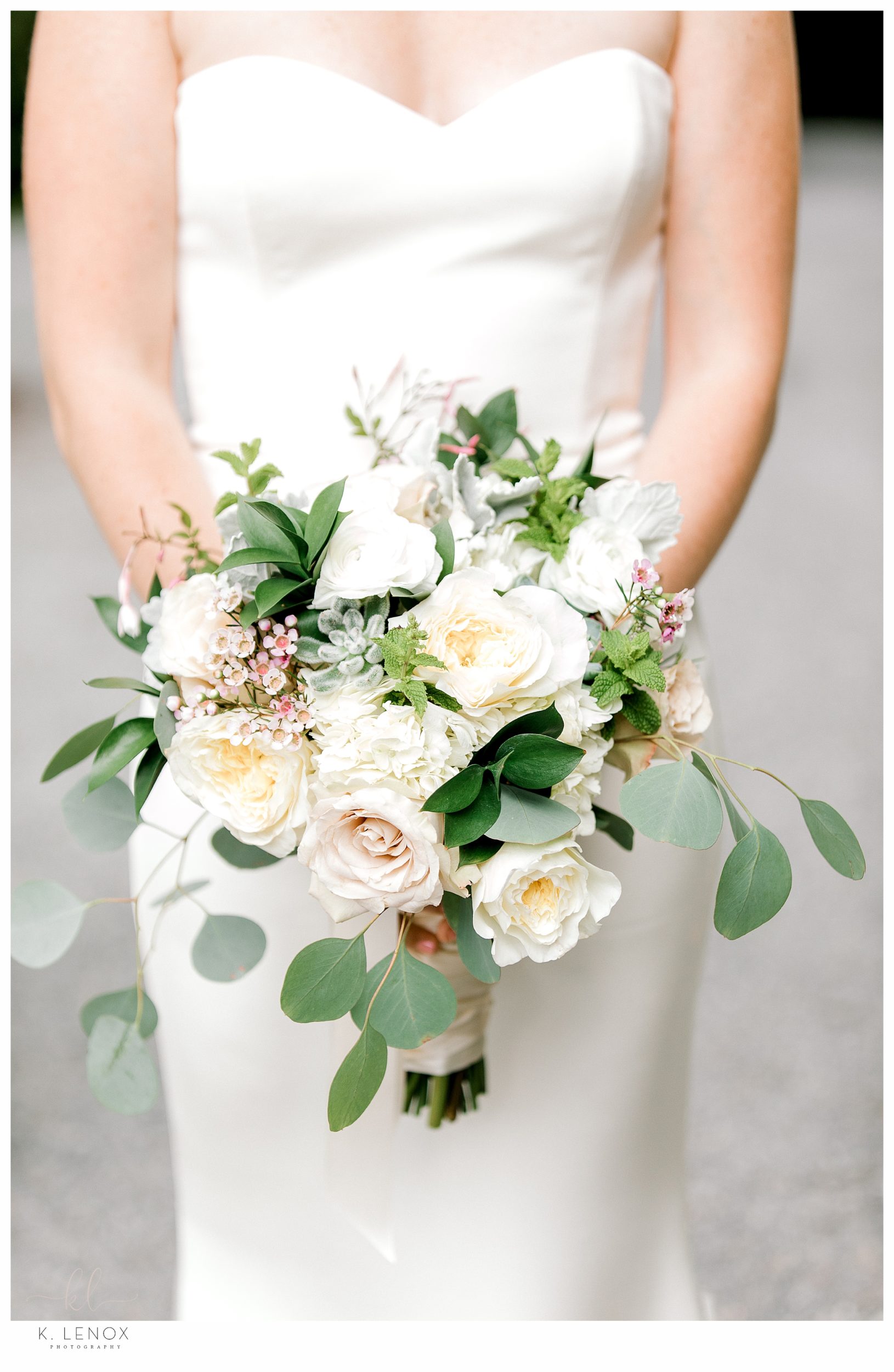 Closeup detail photo of a bridal bouquet with various white flowers and greenery. 